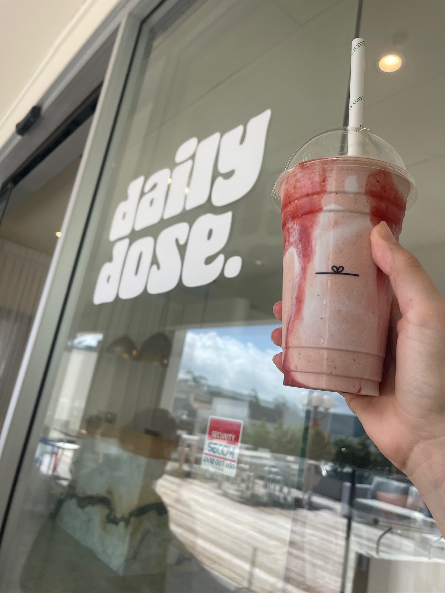 A strawberry dose smoothie held in front of the Daily Dose window logo.