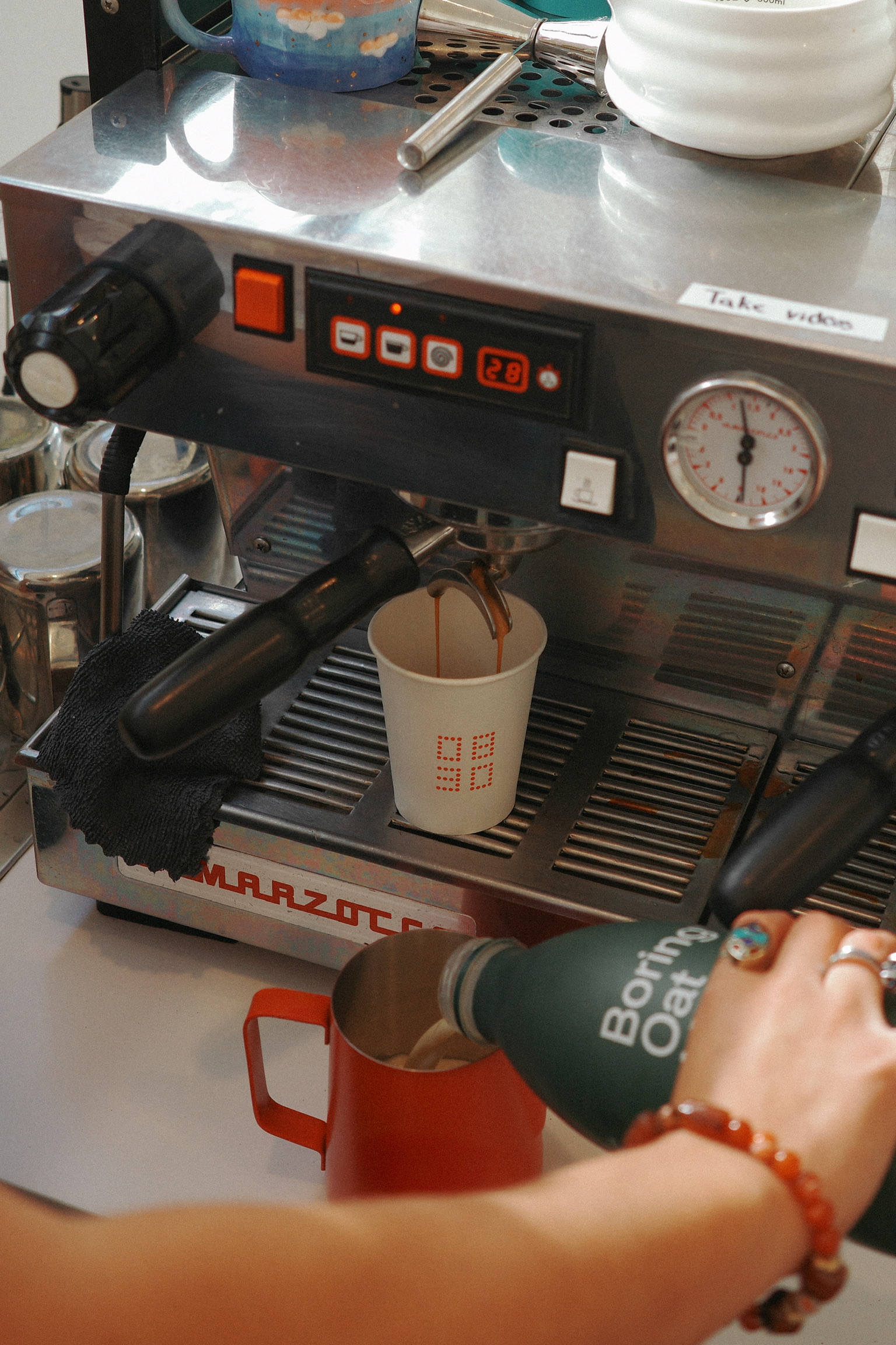 Espresso pulling on the La Marzocco while oat milk is poured into a red pitcher.