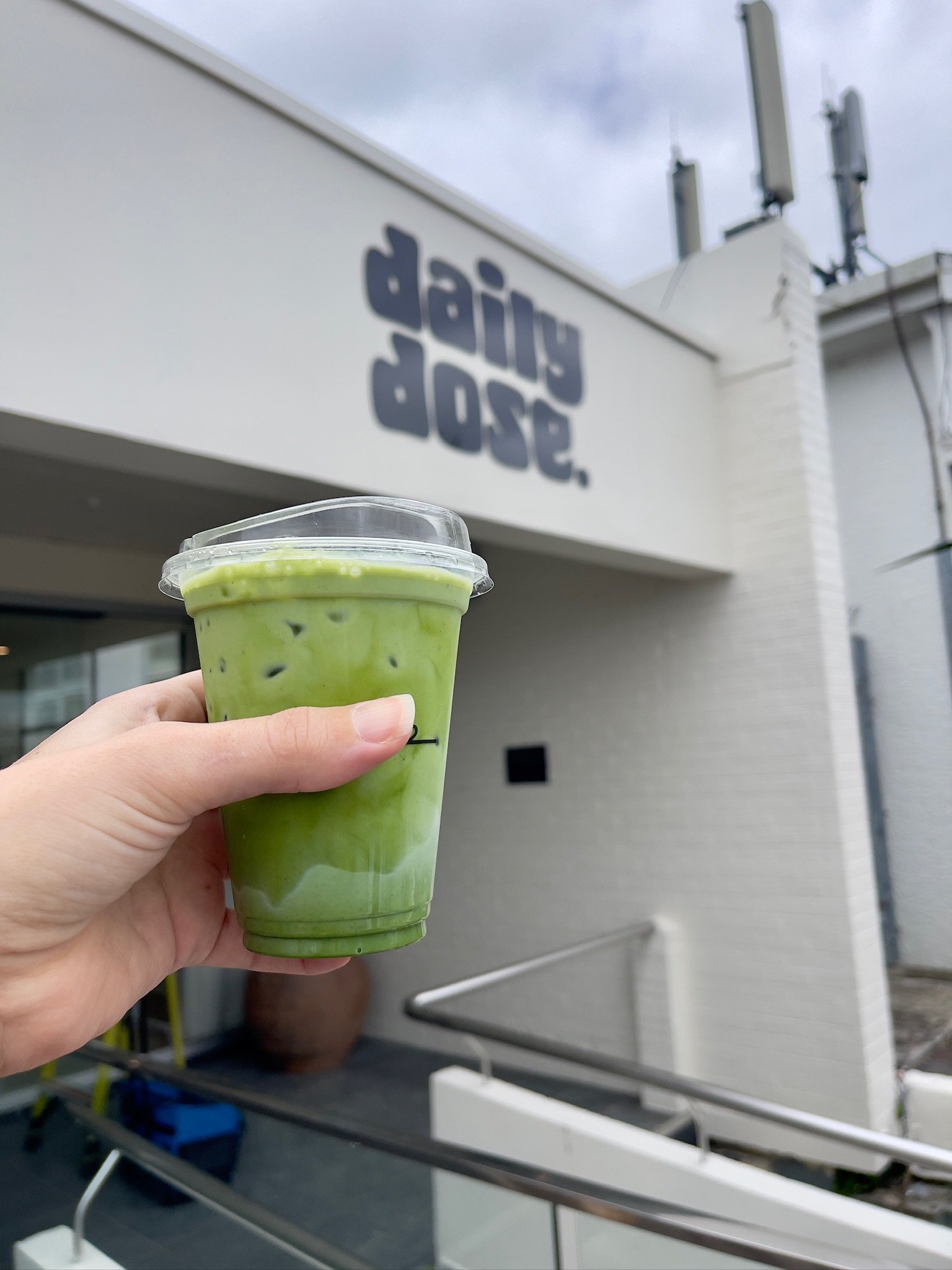 A matcha cloud held in front of the Daily Dose storefront.